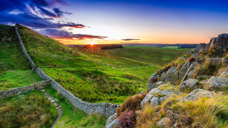 The sun setting on Hadrian's Wall, which is surrounded by green fields and rolling hills near Haltwhistle, England