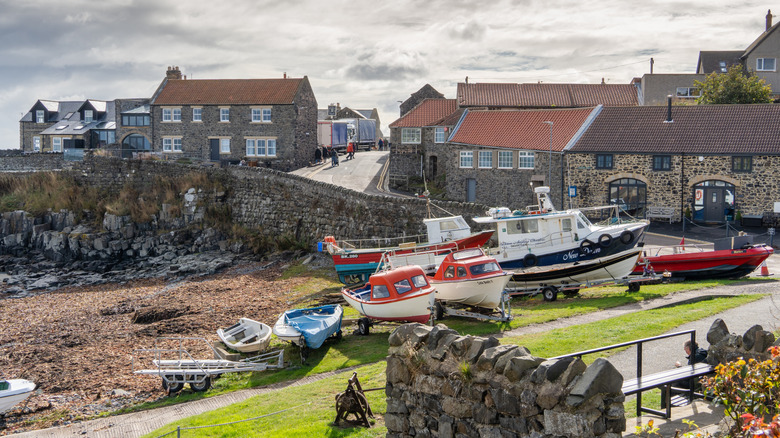 Fishing boats by a pebbly beach, stone wall, and cottages in Craster village, Northumberland