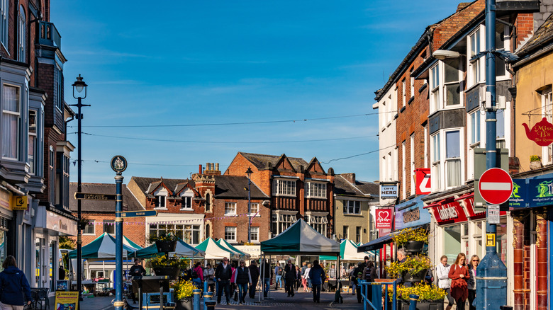 People walking alongside shops and market stalls, Melton Mowbray, Leicestershire, UK.