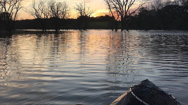 A kayak on the calm water of Duck Creek lake during sunset with shadowy trees in the background.