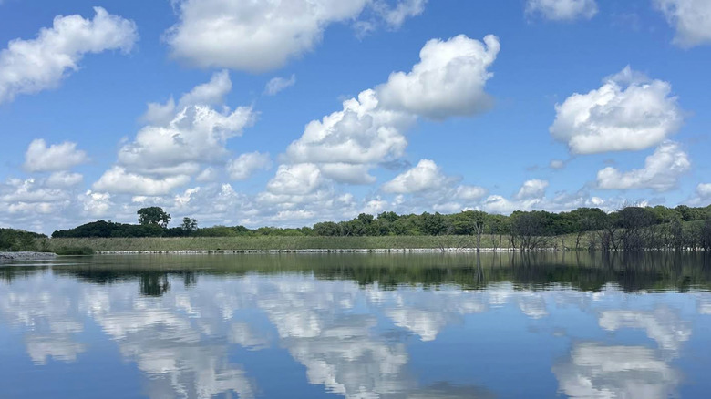 Clouds reflect in the water at Duck Creek Recreation Area, with tree line in the background.