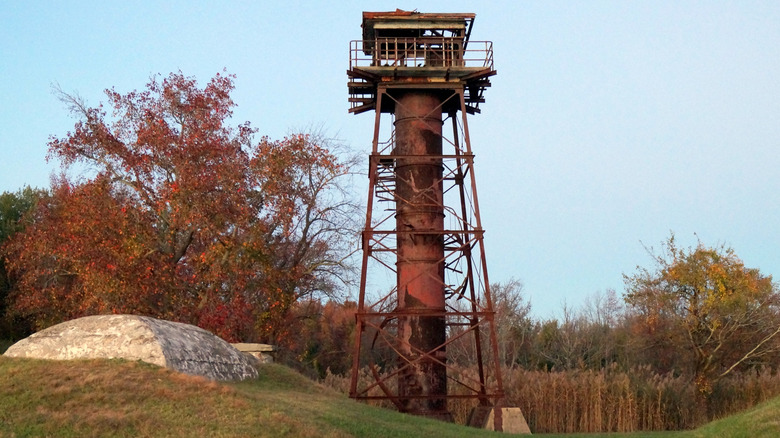 Rusted red metal tower surrounded by fields and autumn trees, under a blue sky