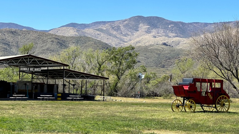 A red stagecoach next to an outdoor dining area with mountains behind Bumble Bee Ranch Adventures