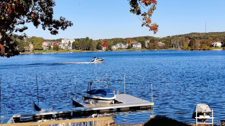 Small boat parked at a dock with a speed boat gliding by in the distance along the blue waters of Deep Creek Lake in Maryland