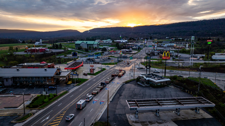 Stretch of Route 30 in Breezewood, mostly empty but with a few trucks, lined in businesses, with sunrise over treed mountains in the background