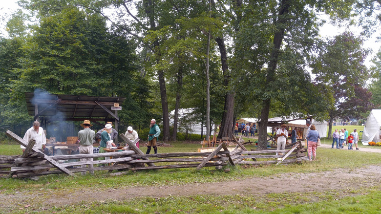 Mountain Craft Days, with people in period and modern dress walking around a wooden fence and booths, surrounded by trees