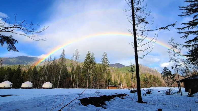 Rainbow over a forested mountain range, meadow, and the yurts of Breitenbush in Oregon