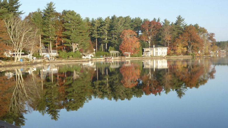 Few buildings and boats lining the shore of Long Pond surrounded by trees on a bright, clear autumn day in Lakeville, MA