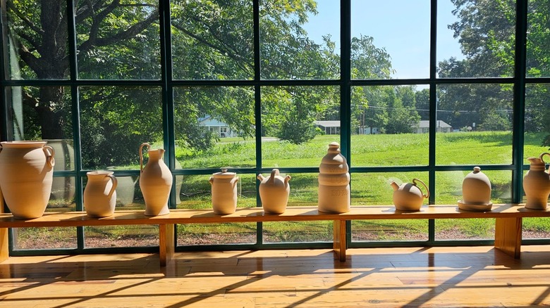 Line of ceramics on a bench in front of window with grass outside North Carolina Pottery Center