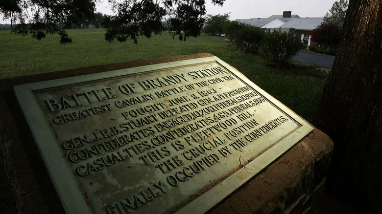Informational plaque at Brandy Station Battlefield, with a green lawn and gray roof in the background