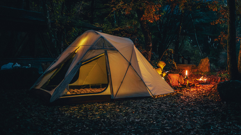 A tent next to a small campfire at night
