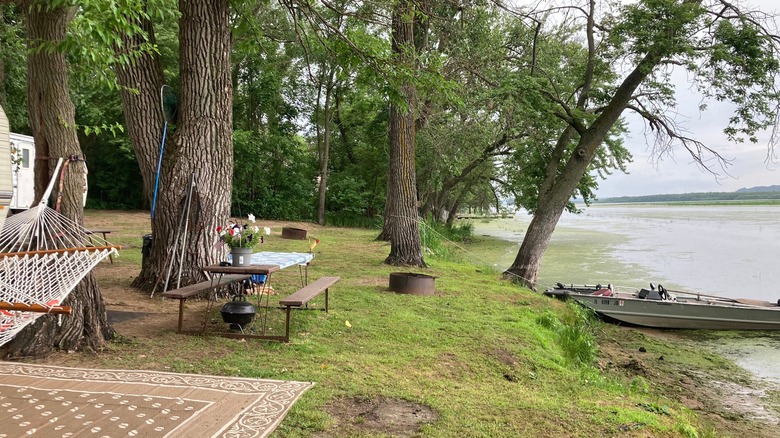 A campsite in the trees with a boat at the river's shore