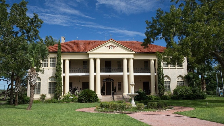 Berclair Mansion just outside Beeville, Texas, with trees on either side and pathway around fountain leading to entrance