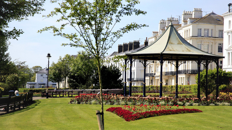 A wrought iron pavilion, flowerbeds, and a lawn in Filey's Crescent Gardens, with white townhouses in the background