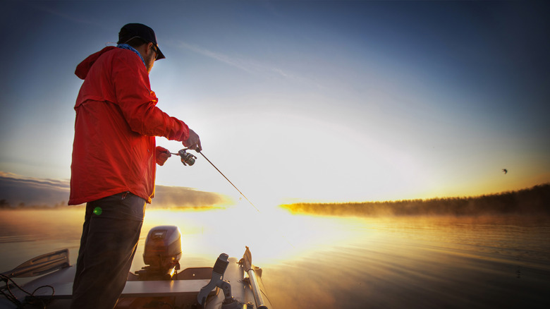 A man fishes from a boat on a lake at sunset