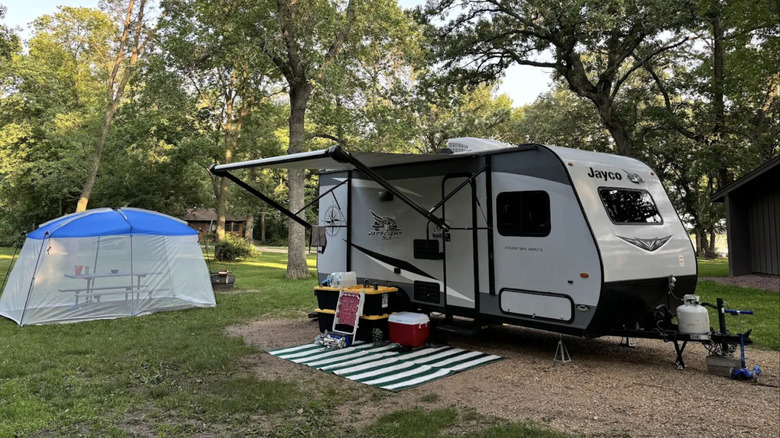 A wooded campsite with a picnic table with a camping trailer.