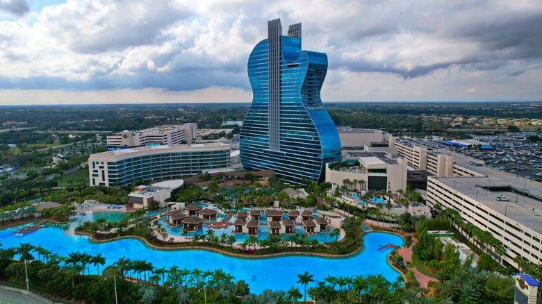 Aerial view of Seminole Hard Rock Hotel & Casino and guitar-shaped building behind pools and other buildings.