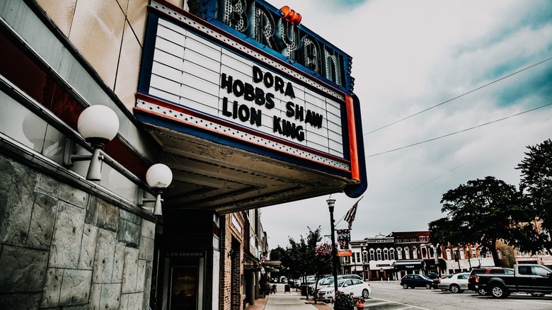 Downtown Bryan, Ohio, with the theater marquee in the foreground and cars parked along a tree-lined street under a cloudy blue sky