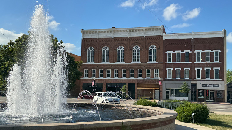 A circular fountain in front of a brown brick building in Bryan, Ohio, with cars and trees in the background under a blue sky