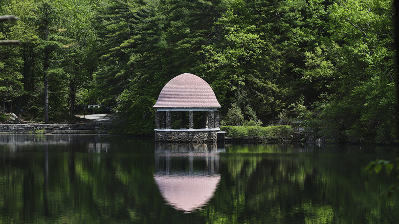 A view of the lake and stone gazebo surrounded by green trees at Coggshall Park in Fitchburg.