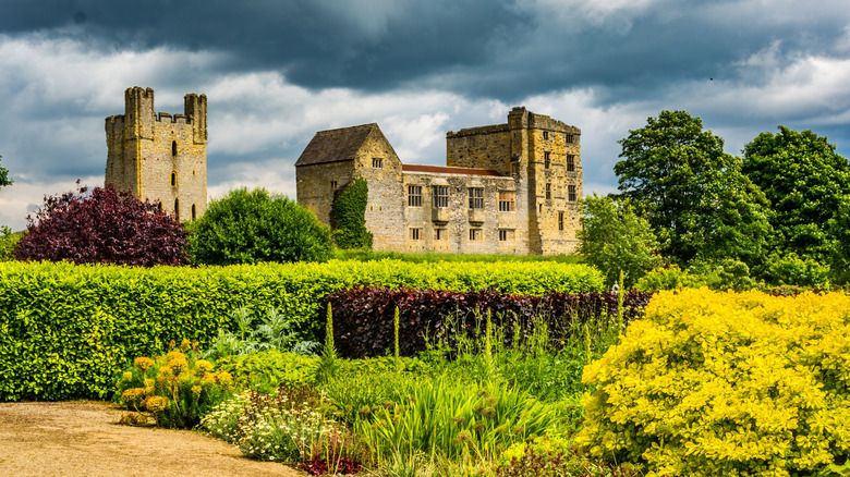 The facade of Helmsley Castle surrounded by gardens on a cloudy day