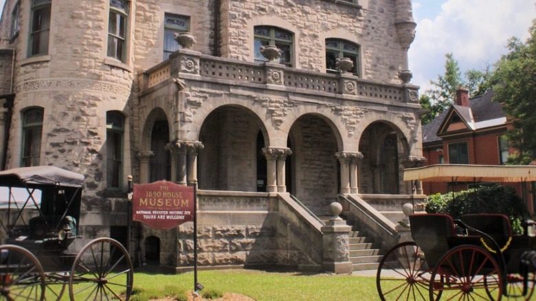 The stone facade of the 1890 House Museum with an arched entry and carriages in front.