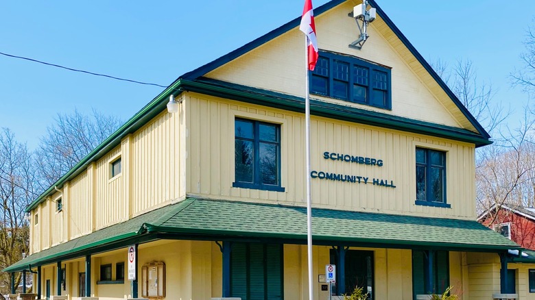 Yellow wooden historic building with Schomberg Community Hall on facade and blue sky