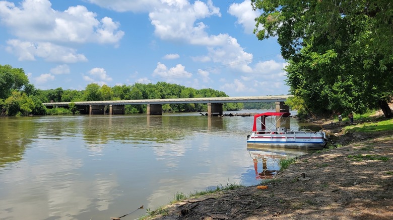 Small boat parked on the banks of a river with a bridge behind it at the Twin Bridges Area at Grand Lake State Park, Oklahoma