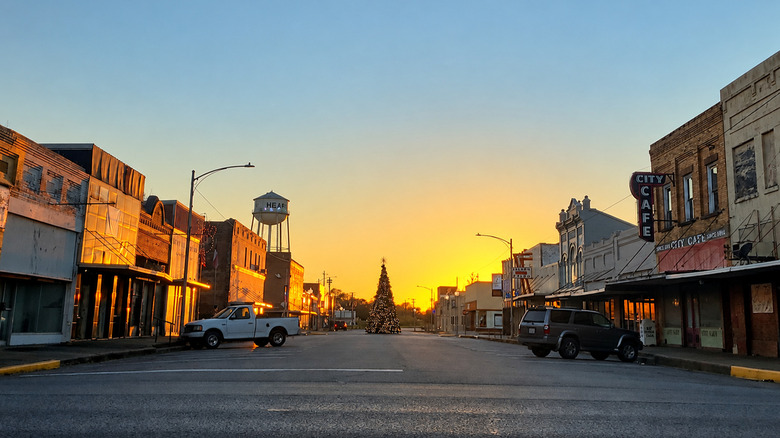 Downtown Hearne, Texas, at sunset, with historic storefronts, parked vehicles, a water tower, and a lit Christmas tree in the center of the street