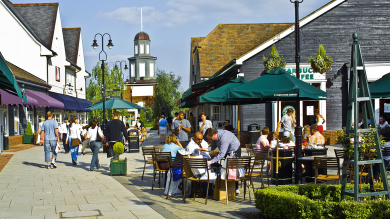 The streets Bicester Shopping village in Oxfordshire England UK on a sunny day with people sitting at cafes