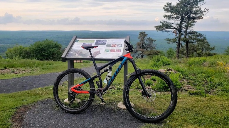 A mountain bike parked next to a sign on top of Camelback Mountain in Pennsylvania, with views of rolling hills in the background.
