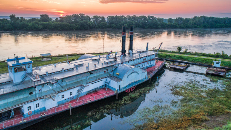 the sun rises beyond the trees along the Missouri River, where the Captain Meriwether Lewis Dredge is docked