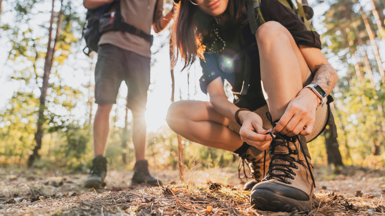 A person tying their shoe in the woods on a hike