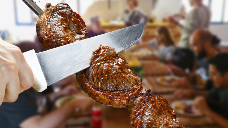 A Gaucho at a Brazilian steakhouse slicing picanha off a skewer in the dining room