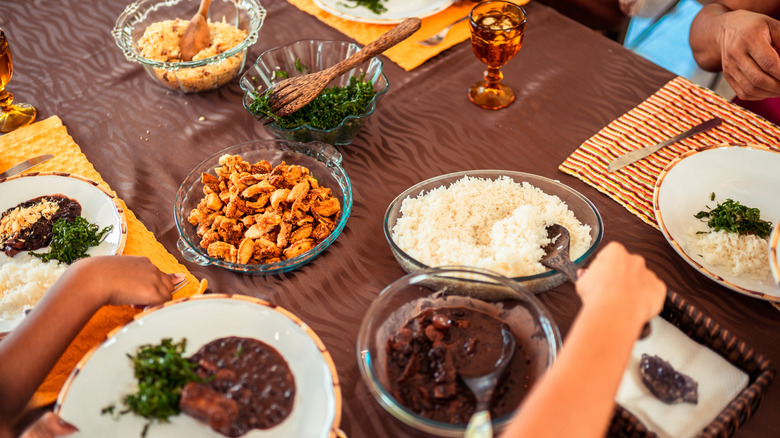 A home dinner table in Brazil, with hands serving up feijoada