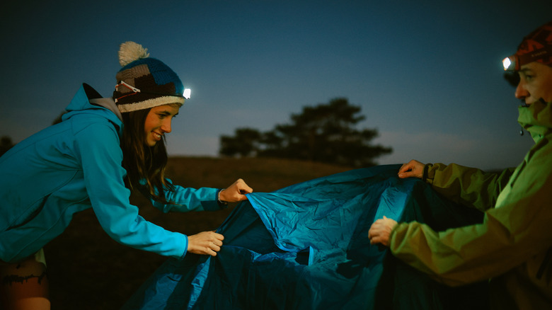 two people with headlamps on setting up tent