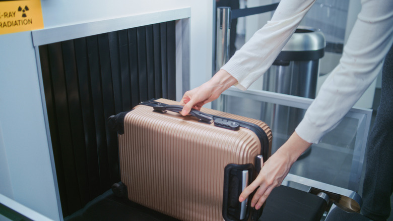A person putting a carry-on suitcase through an X-ray machine at security