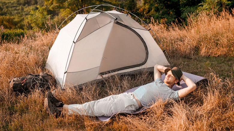 A hiker laying on the grass near his tent and looking relaxed