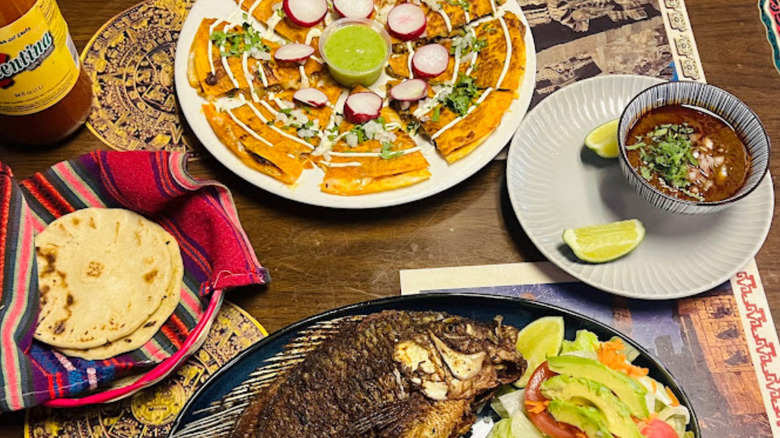 A table filled with authentic Mexican food dishes, including whole fried tilapia, a quesadilla, soup, and tortillas
