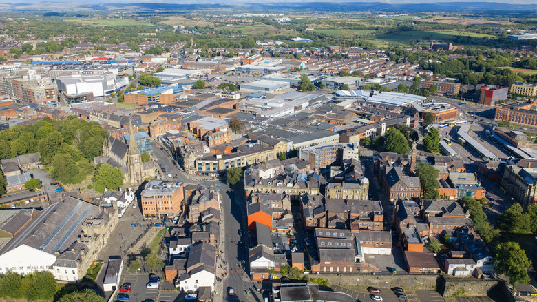 High-angle aerial image overlooking Bury Parish Church, marketplace retail buildings, the transport interchange, and surrounding Lancashire countryside