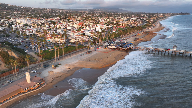Aerial view of ocean waves moving high up a California beach, consuming most of the shoreline, with houses and buildings nearby.
