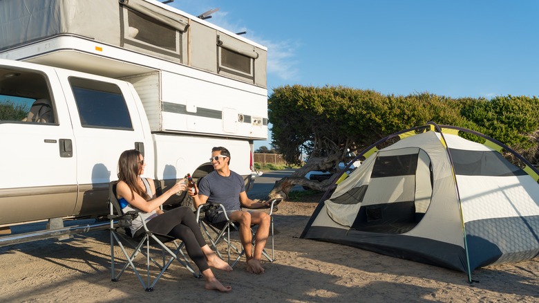 A couple relaxing next to their tent and truck camper at a campsite
