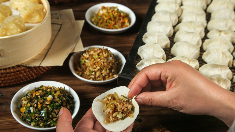 A picture of dumplings being made with the bowls of filling and a tray in the background