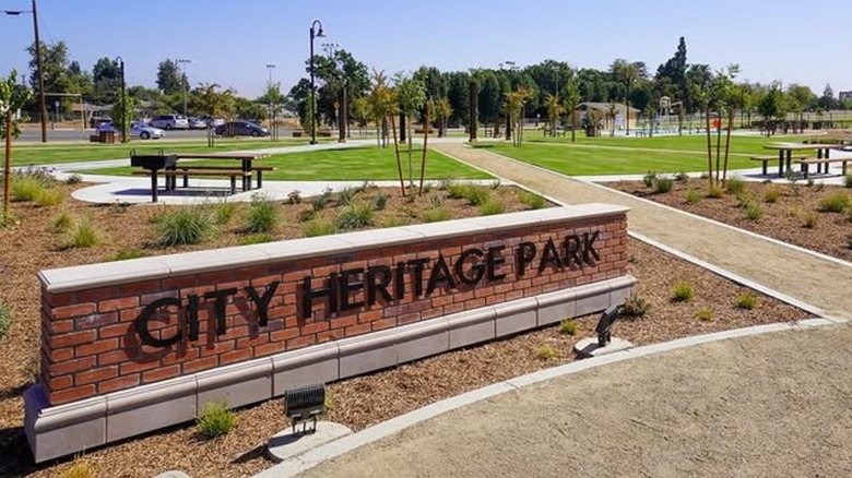 Green area with small picnic area in the background and a brick sign reading "City Heritage Park" in the foreground, Parlier