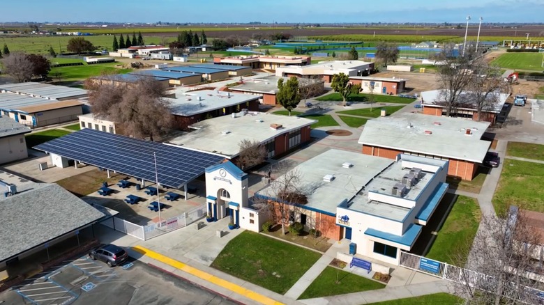 Aerial view of a school campus with white-roofed buildings, solar panels, and sports fields in Parlier, near Fresno