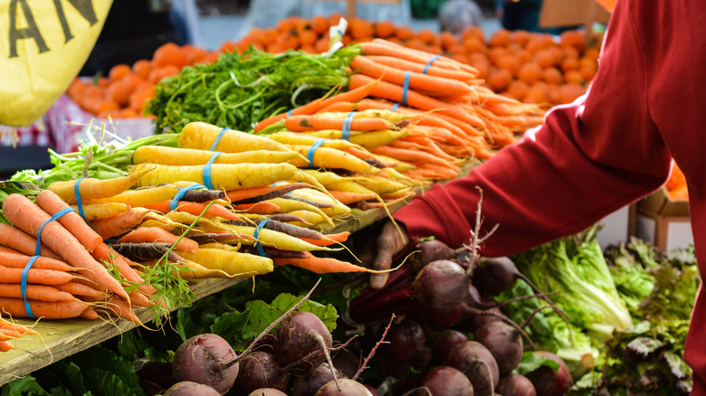 A woman grabbing fresh carrots and beets at a Sacramento farmers market