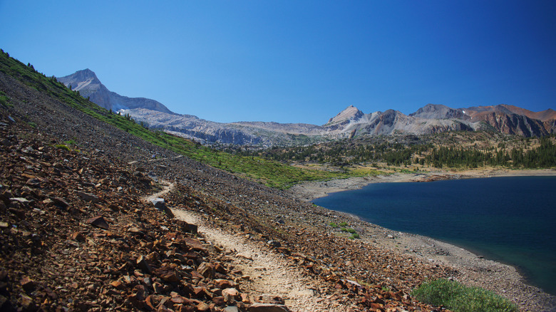 A hiking trail passes a lakeside with high mountains behind