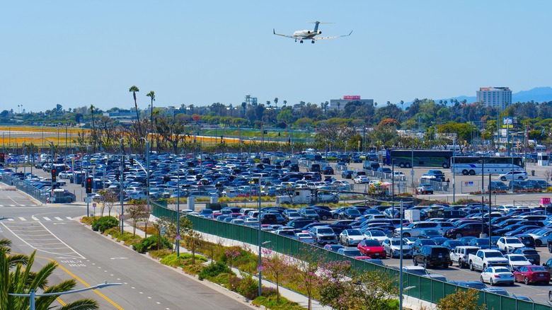 A plane flies over a full LAX parking lot