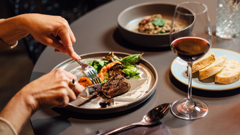 Elegant restaurant dining scene featuring ostrich fillet with grilled vegetables, fresh salad, and red wine, captured in a sophisticated, modern setting