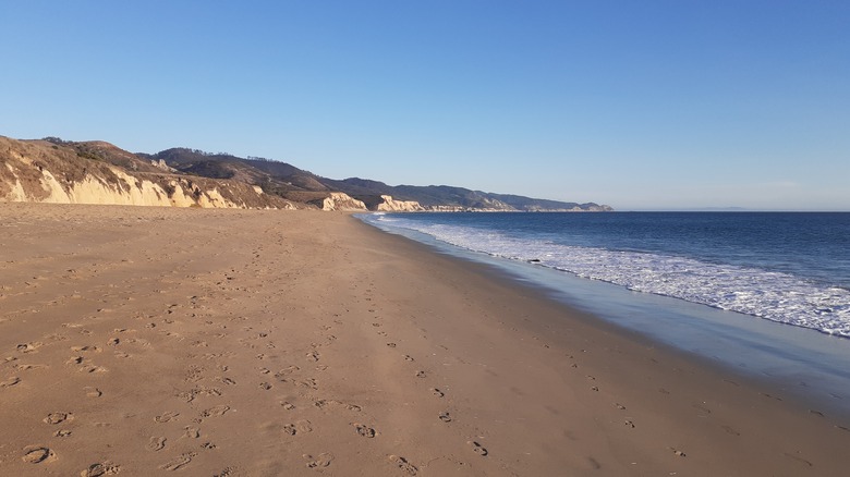 Beach with visible footprints in the sand and sea bluffs in the background